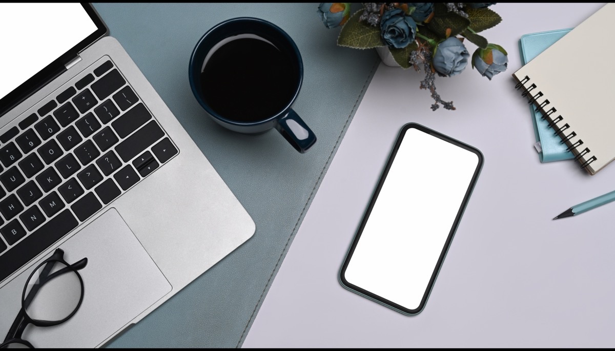 A phone, laptop and notebook arranged on a desk