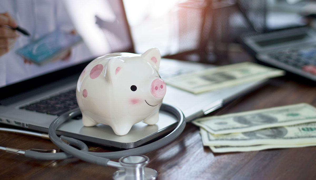 A piggy bank and stethoscope next to cash and a calculator on a desk, representing health savings account spending